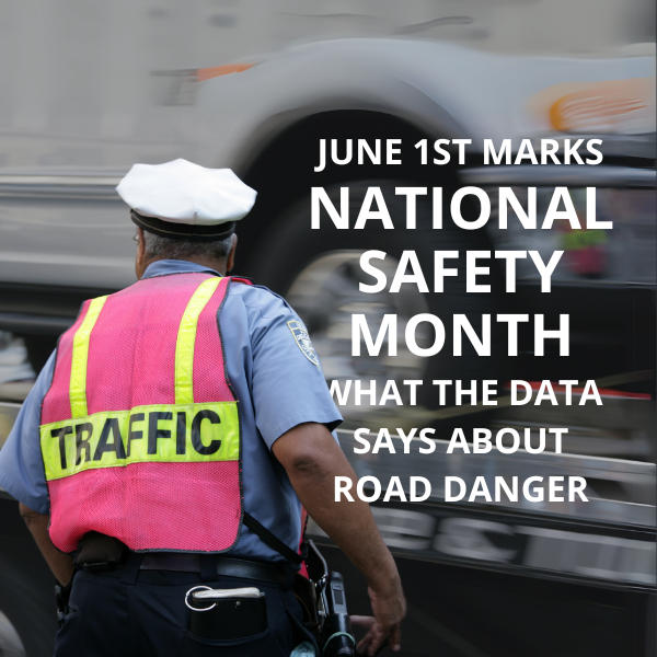 A city traffic officer stands in the center of a busy intersection surrounded by cars and buildings. Overlaid text in the center of the image reads “June 1st Marks National Safety Month.”