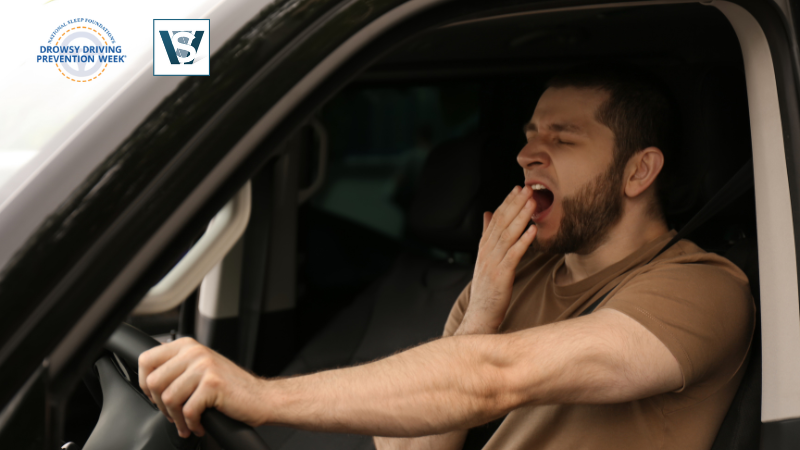 Tired driver yawning behind the wheel during Drowsy Driving Prevention Week, highlighting the dangers of fatigue on the road